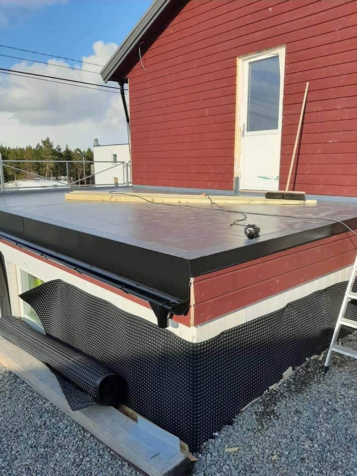 A flat roof edge finished in black membrane against red cladding