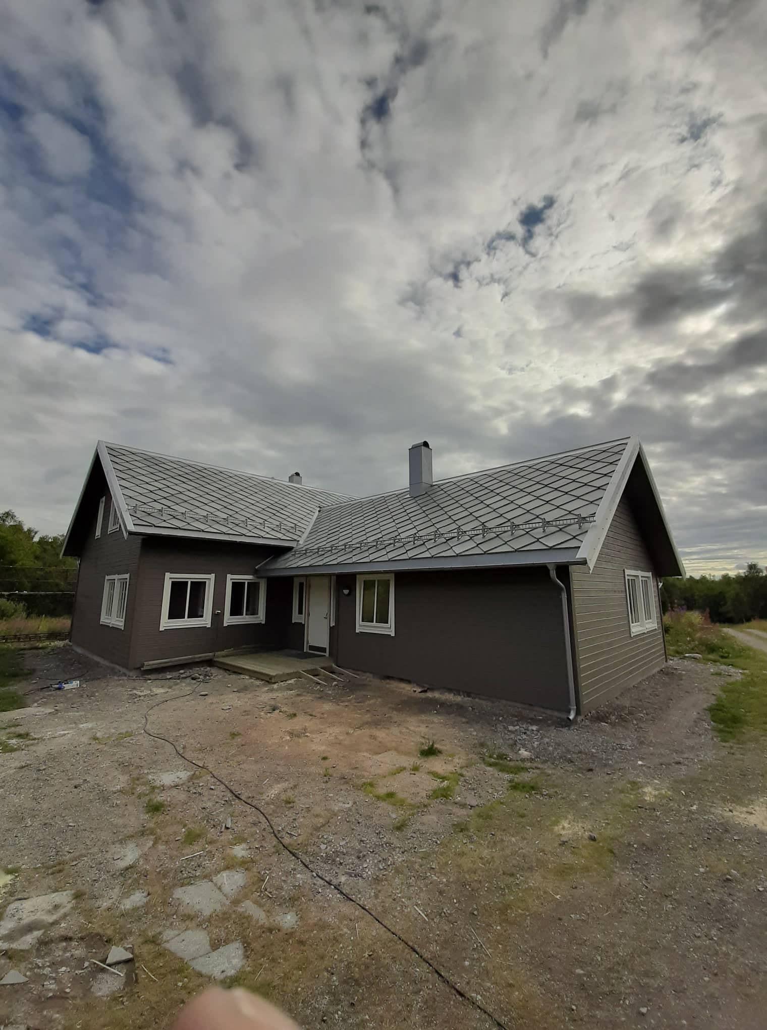 A grey house with a dark roof on open ground under a cloudy sky