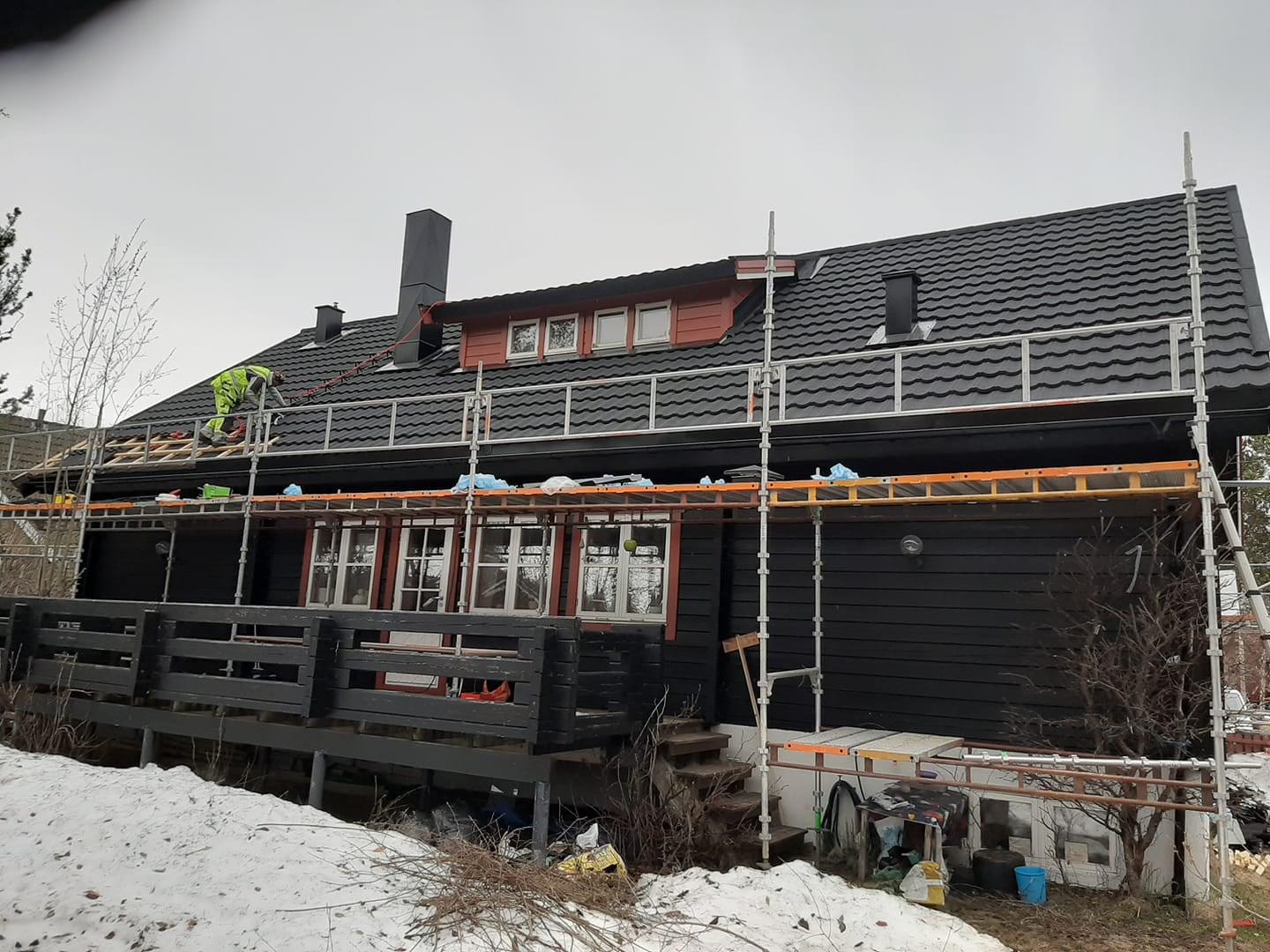 A dark timber house with scaffolding along the eaves and a new black roof, snow on the ground